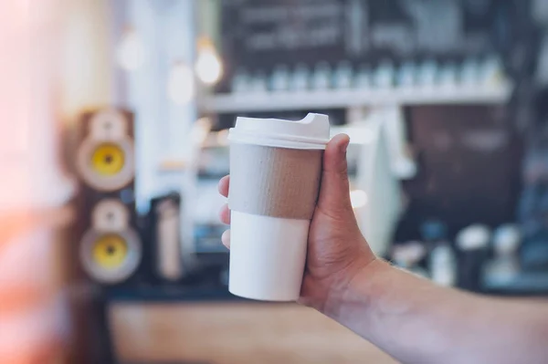 Mock-up of a cardboard glass for coffee in a guy\'s hand against the background of a bar in a cafe