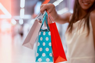 Elbiseli genç bir kadın elinde güzel ve parlak hediye çantalarıyla süpermarkette yürüyor.