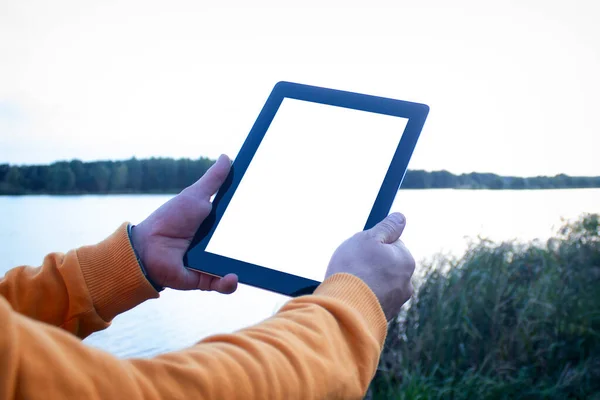 Mock up image of a Man holding black tablet in hand with blank white screen on background river