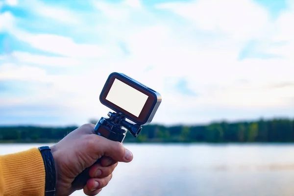 Tourist shoots a video on an action camera against the backdrop of nature and the river. Close-up of a white screen mockup on the camera