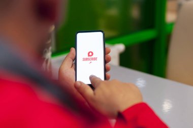 Video kanalına abone ol. Beyaz akıllı telefon ekranındaki eylem simgesini ara. Adam telefon ekranında bir düğmeye basıyor.