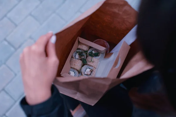 The girl opens a cardboard bag with a set of sushi and ginger. Seafood delivery concept