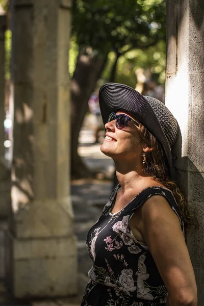 Middle aged woman leaning against a column with sunbeams on her face