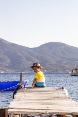 Sırtında okyanusa bakarak otururken bir dock üzerindeki küçük çocuk