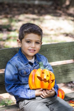 Küçük çocuk bir bankta bir kabak ile Cadılar Bayramı'nda oturmuş.