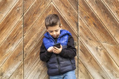 Ahşap kapı arka plan ile bir mibile telefon ile küçük çocuk