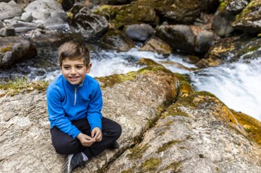 Vahşi bir nehrin yakınında oturan sevimli litle çocuk