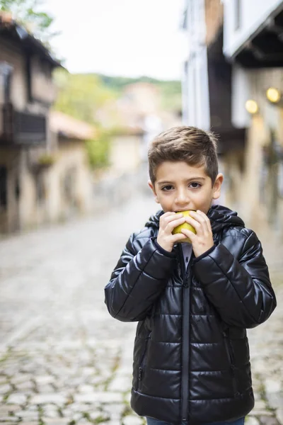 Bellissimo ragazzo mordere una mela per strada — Foto Stock
