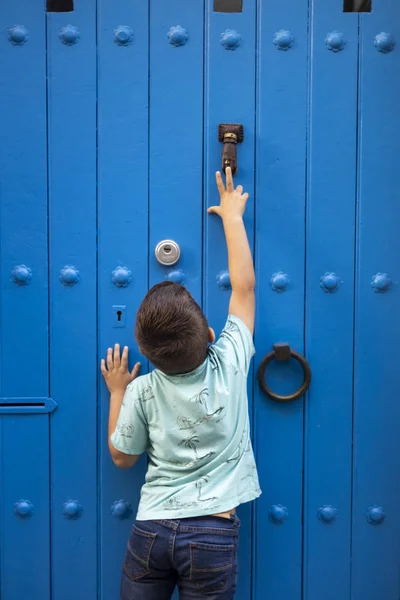 Kleiner Junge versucht an eine blaue Tür zu klopfen — Stockfoto