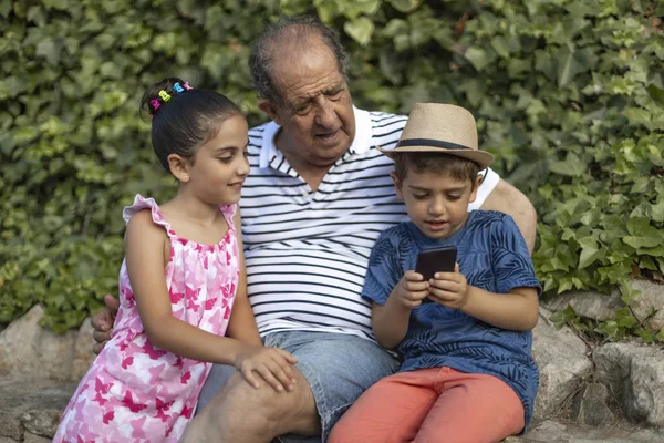 Avô e netos brincando com um telefone celular — Fotografia de Stock