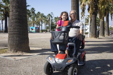 Grandfather and granddaughter driving a motorized chair clipart