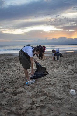 Bir grup çocuk plajda plastik topluyor. 