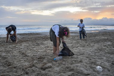 Bir grup çocuk plajda plastik topluyor. 