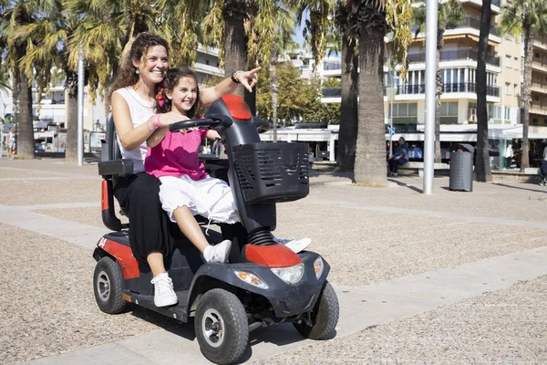 Mãe e filha em uma cadeira motorizada na rua — Fotografia de Stock
