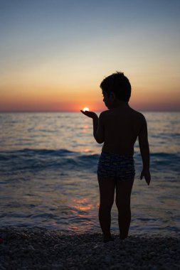 Little kid playing with the sun on the beach at sunset clipart