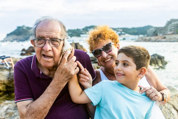 Büyükbaba ve torun sahilde deniz kabuğuyla oynuyorlar.