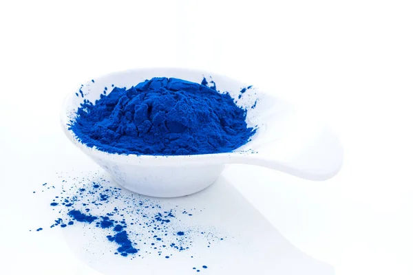 Espirulina azul en polvo en cuchara blanca aislada sobre fondo blanco. Extracto de Phycocyanin. Superalimento natural, vegetariano, suplemento dietético saludable. Imagen De Stock