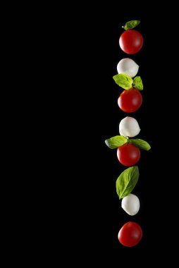 Dikey mozzarella peyniri, taze kiraz domatesi ve fesleğen yaprakları siyah zemin üzerinde izole edilmiş yansıma, sağlıklı gıda konsepti yatay görüntü ve metin için boşluk.