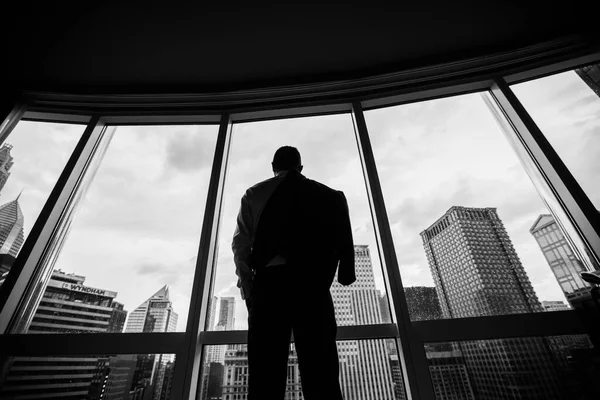 The man puts on a jacket. He stands with his back. Panoramic windows. The landscape of the city and skyscrapers opens.