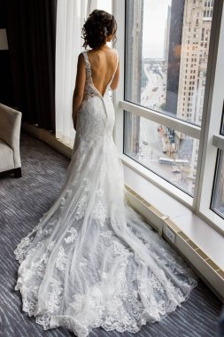 Gelinlik giymiş gelin pencerenin yanında duruyor ve elbiseyi omuzlarının üzerine indirdi. Harika ışık..