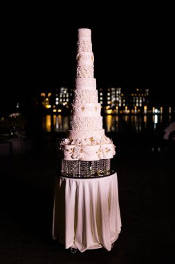 Düğün pastası masanın üstünde duruyor. Çiçeklerin etrafında. Dışarıda.