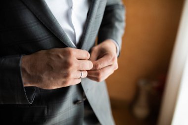 Bir adamı giydirmek. Düğmeleri bağlar. Pencerenin yanında duruyor..