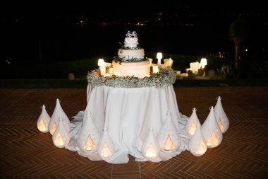 Düğün pastası masanın üstünde duruyor. Çiçeklerin etrafında. Dışarıda.