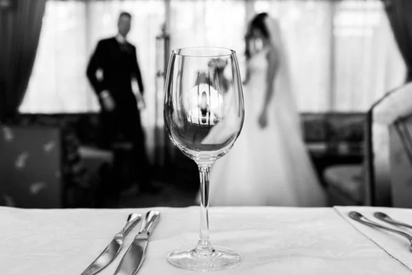 手前には空のワインと刃物のグラスがある 背景にはカップル — ストック写真
