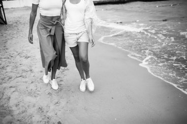 İki kadın kıyı boyunca yürür. Beyaz spor ayakkabılarla. Su görünür..