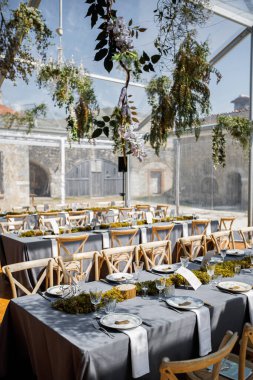 Tabaklar, bıçaklar ve çatallarla süslenmiş düğün masası, mum, yosun ve yeşillik.