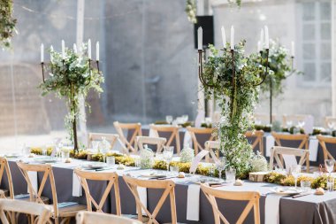 Tabaklar, bıçaklar ve çatallarla süslenmiş düğün masası, mum, yosun ve yeşillik.