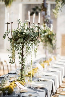Tabaklar, bıçaklar ve çatallarla süslenmiş düğün masası, mum, yosun ve yeşillik.