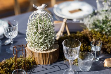 Tabaklar, bıçaklar ve çatallarla süslenmiş düğün masası, mum, yosun ve yeşillik.