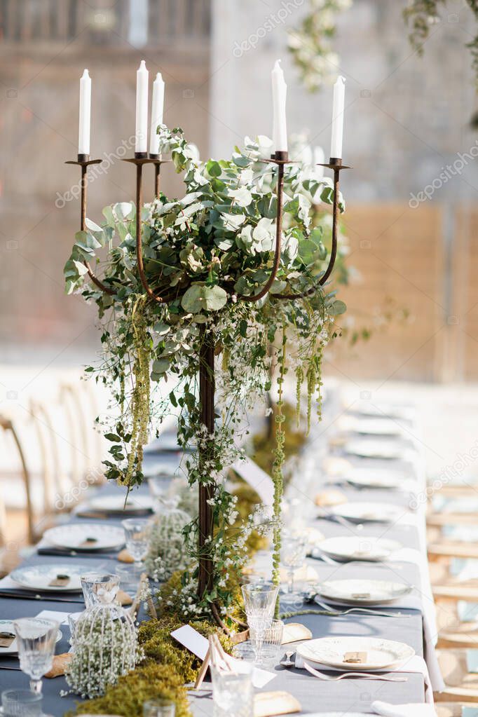 wedding table decorated by plates, knives and forks, candle, moss and greenery