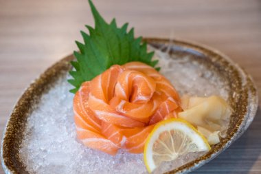 Bir restoranda servis edilen bir kasede sebze ve buz ile gül şeklinde somon saşimi