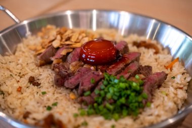 Sarımsaklı kızarmış pirinçli biftek, üzerine az pişmiş sığır eti ve tavada balık soslu yumurta sarısı.