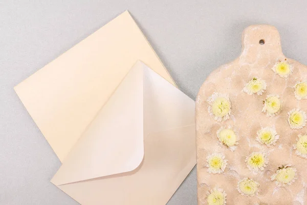 Envelope, note with place for text and decorative board with small yellow flowers on gray sparkled background. Mockup envelope with flowers and a letter, greeting card for Valentines Day or wedding with place for your text. Flat lay, topview mock-up.