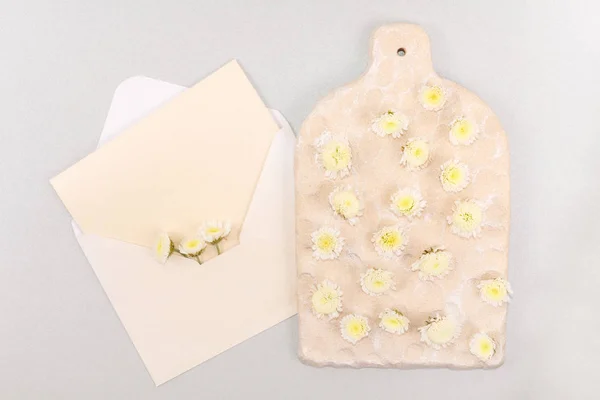 Mockup envelope with flowers and a letter, greeting card for Valentines Day or wedding with place for your text. Flat lay, topview mock-up. Envelope, note with place for text and decorative board with small yellow flowers on gray sparkled background.