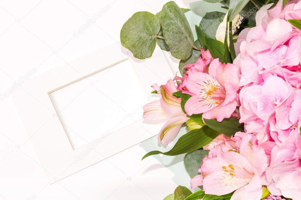 Mock-up Composition of tender flowers and white frame in classic style. A gift for St. Valentine's Day with a place for your text. Flat lay, top view photo mock-up. Tender flowers and white frame mock-up.