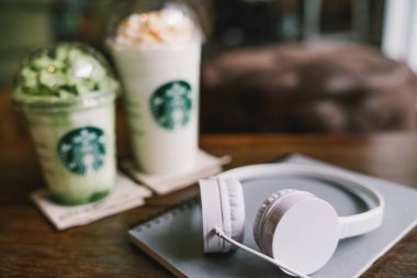 Bangkok, Tayland - 30 Ağustos 2018: Beyaz kulaklık ve Starbucks Coffee, masada iki frappucino içecekler içinde geçmiş üstünde defter. İllustratative yazı işleri