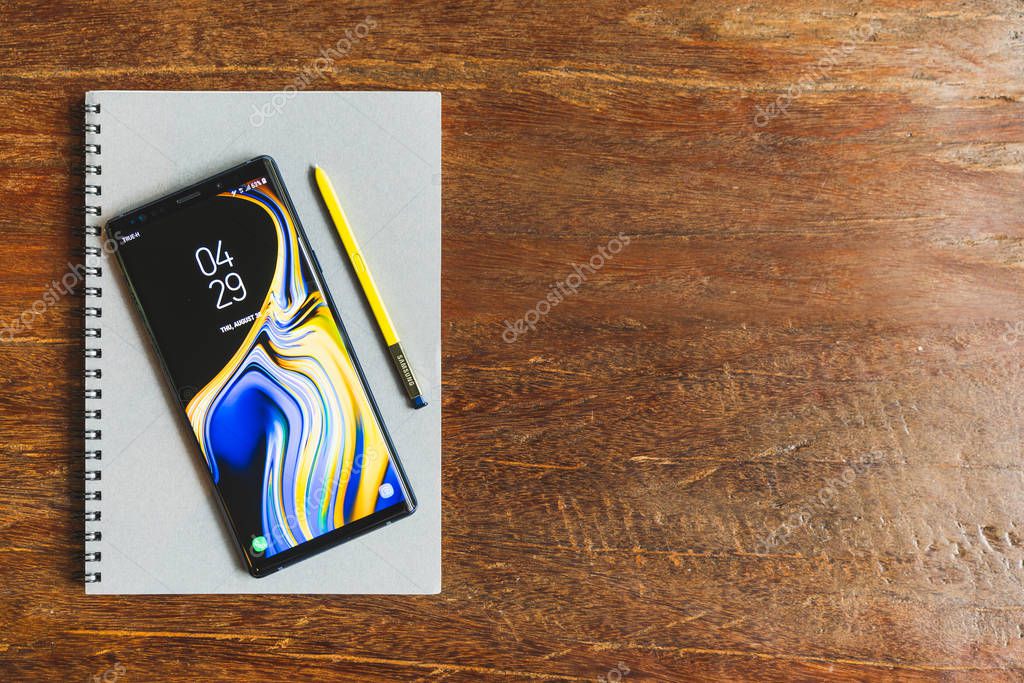 Bangkok, Thailand - Aug 30, 2018: Ocean Blue Samsung Galaxy Note 9 with yellow S pen stylus on a notebook with copy space on wooden table. Illustrative Editorial.