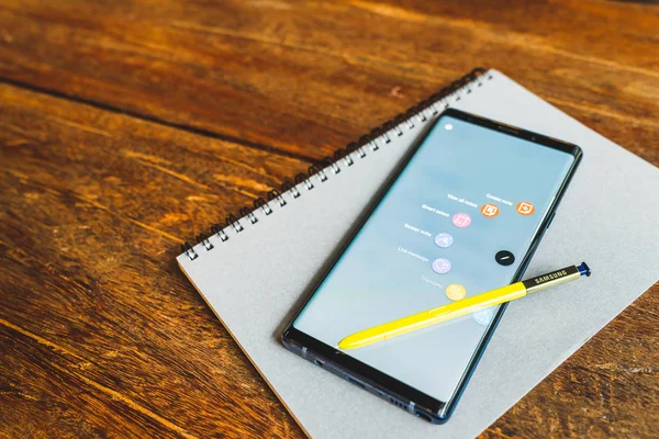 Bangkok, Thailand - Aug 30, 2018: Ocean Blue Samsung Galaxy Note 9 with yellow S pen stylus on a notebook, copy space on wooden table. Screen displaying note and drawing apps. Illustrative Editorial.