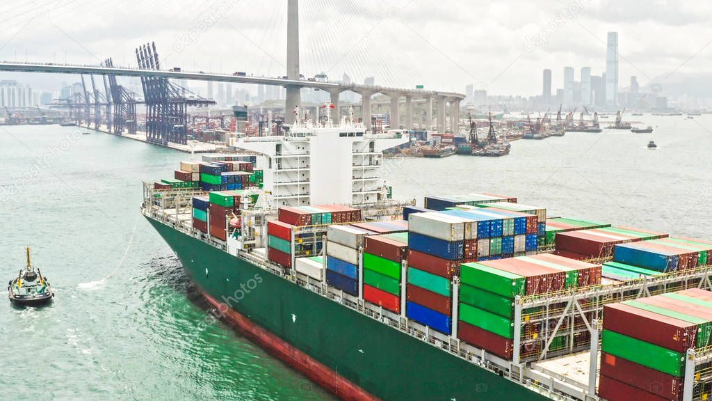Large cargo ship transporting shipment container arriving Hong Kong port, bridge and city background, drone aerial view. Freight transportation, import export business or industrial concept