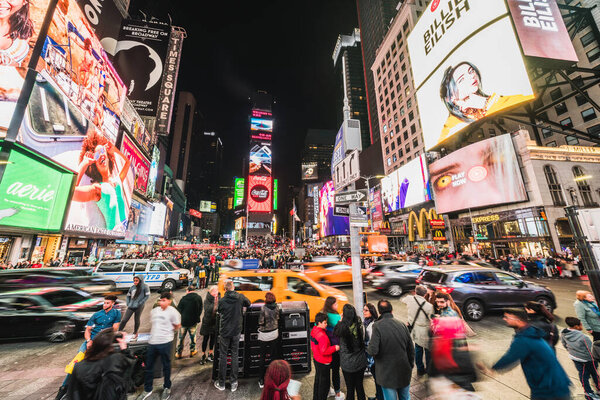 New York City, United States - Mar 31, 2019: Crowded people, car traffic transportation and billboards displaying advertisement at night in Times Square. American lifestyle or modern city life concept