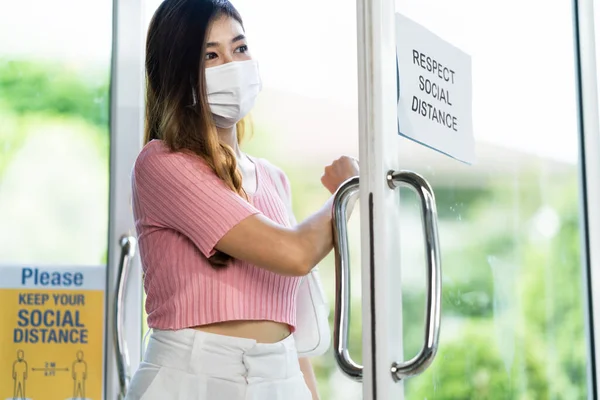 Asian woman wear face mask entering shop or restaurant, open entrance door with forearm or elbow. Hygienic new normal lifestyle and social distancing concept