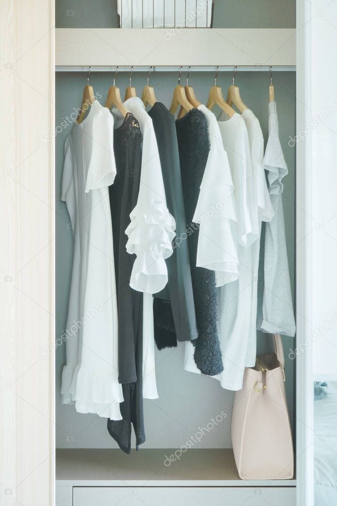 Black and white cloths hanging in white wooden wardrobe