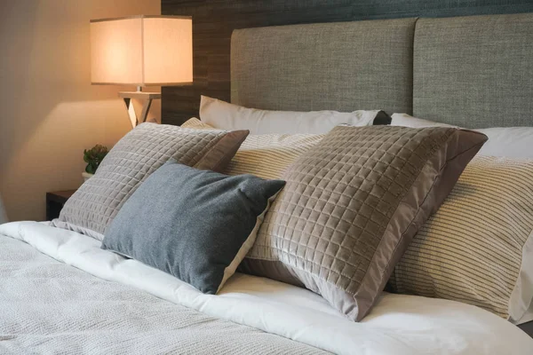 Almohada gris y marrón en la cama con lámpara de lectura en el fondo — Foto de Stock