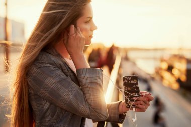 Telefonunu günbatımı arka plan ile güzel kız konuşma