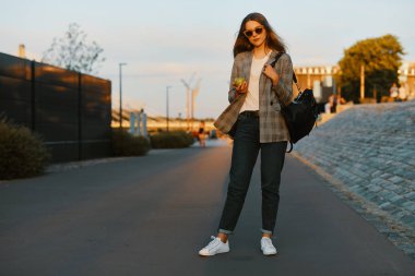 Moda kız yürüyüş günbatımı arka plan ile sokakta