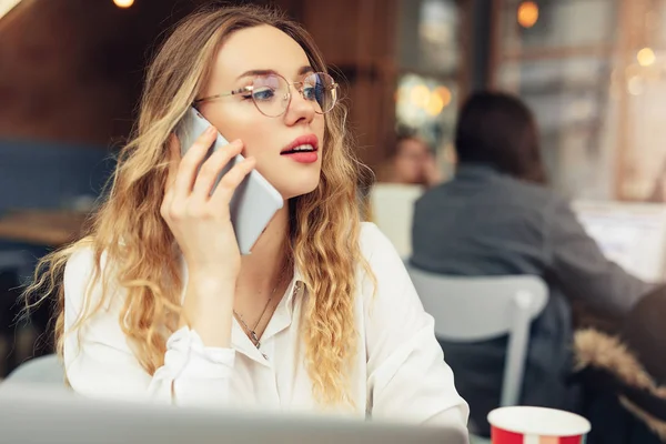 Woman Wear Glasses, Talk At Phone, Drink Her Hot Coffee While Work In Cafe On Her Laptop. Portrait Of Stylish Smiling Woman In Winter Clothes Drinking Hot Coffee And Work At Laptop. Female Winter Style. - Image